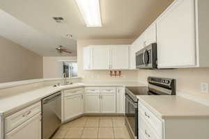 Kitchen featuring stainless steel appliances, light tile patterned flooring, a sink, and white cabinets