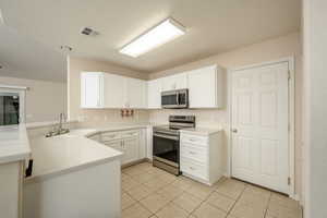Kitchen featuring appliances with stainless steel finishes, a peninsula, a sink, light tile patterned flooring, and white cabinets