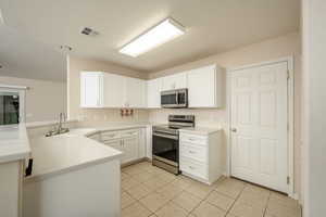 Kitchen with stainless steel appliances, a sink, a peninsula, light tile patterned floors, and white cabinetry