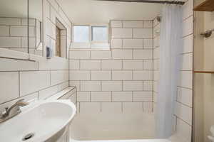 Full bath with a sink, shower / tub combo with curtain, tile walls, and tasteful backsplash
