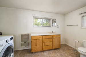Bathroom featuring washer / dryer, heating unit, toilet, stone finish flooring, and baseboards