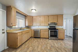 Kitchen with a sink, stainless steel appliances, under cabinet range hood, light countertops, and light wood finished floors