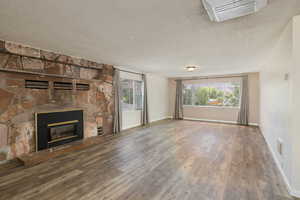 Unfurnished living room with wood finished floors, a stone fireplace, a textured ceiling, and baseboards