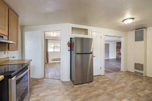 Kitchen featuring appliances with stainless steel finishes, a heating unit, baseboards, brown cabinetry, and glass insert cabinets