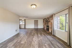 Unfurnished living room with wood finished floors, a stone fireplace, and baseboards