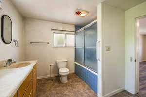 Full bathroom featuring toilet, enclosed tub / shower combo, vanity, and baseboards