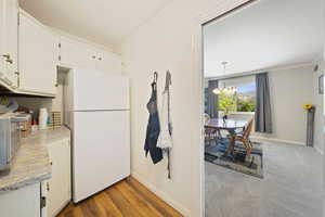 Kitchen featuring white appliances, a chandelier, baseboards, white cabinetry, and wood finished floors
