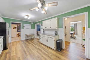 Kitchen with stainless steel fridge, ceiling fan, white cabinets, light wood-style floors, and crown molding