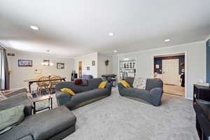 Carpeted living area featuring ornamental molding, a chandelier, recessed lighting, and baseboards