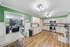 Kitchen with appliances with stainless steel finishes, ornamental molding, wainscoting, white cabinets, and light wood-type flooring