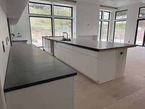 Kitchen featuring dark countertops, white cabinets, modern cabinets, a kitchen island with sink, and light wood finished floors