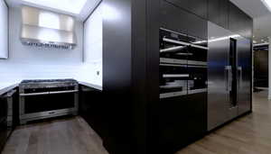 Kitchen featuring stainless steel stove, wall chimney exhaust hood, modern cabinets, light wood-style floors, and dark cabinetry