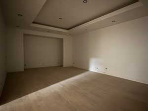 Unfurnished room with a raised ceiling, light wood-type flooring, and recessed lighting