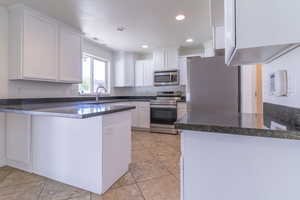 Kitchen with appliances with stainless steel finishes, a peninsula, white cabinetry, a sink, and recessed lighting