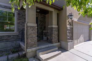 Entrance to property with stone siding, stucco siding, and a garage