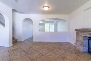 Unfurnished living room featuring a fireplace, a textured ceiling, stairs, baseboards, and tile patterned floors