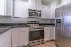 Kitchen with appliances with stainless steel finishes, white cabinetry, and dark stone counters