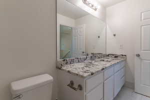 Half bathroom with marble finish floors, toilet, and vanity