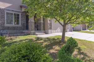 View of front of property featuring driveway, stucco siding, stone siding, and a front lawn