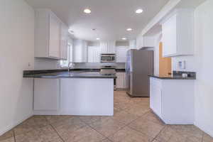 Kitchen with appliances with stainless steel finishes, a peninsula, white cabinets, recessed lighting, and baseboards