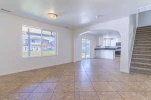 Unfurnished living room with arched walkways, stairs, light tile patterned floors, and a textured ceiling