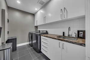 Clothes washing area with separate washer and dryer, cabinet space, baseboards, dark tile patterned floors, and recessed lighting