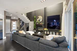 Living area featuring stairway, a glass covered fireplace, wood finished floors, baseboards, and recessed lighting