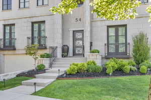 Doorway to property featuring french doors, an attached garage, a lawn, and stone siding