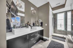 Bathroom featuring a chandelier, a shower stall, double vanity, baseboards, and tile patterned floors