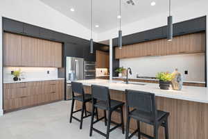 Kitchen featuring stainless steel refrigerator with ice dispenser, modern cabinets, a sink, a kitchen bar, and recessed lighting