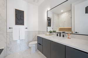 Bathroom with tile walls, marble finish flooring, toilet, vanity, and a wainscoted wall