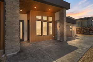 Rear view of house featuring driveway, an attached garage, stone siding, and stucco siding