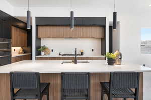 Kitchen with modern cabinets, a sink, light countertops, decorative backsplash, and brown cabinets