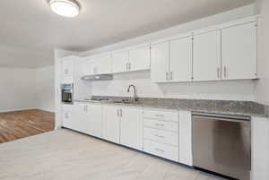 Kitchen featuring stainless steel appliances, under cabinet range hood, a sink, and white cabinetry