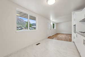 Kitchen with white cabinets, light marble finish floors, stainless steel oven, cooktop, and baseboards