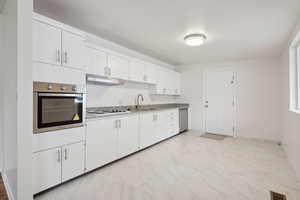 Kitchen featuring stainless steel appliances, under cabinet range hood, white cabinets, a sink, and light marble finish flooring