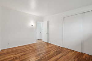 Unfurnished bedroom featuring wood finished floors, a closet, and baseboards