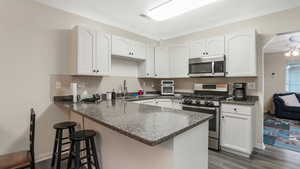 Kitchen with stainless steel appliances, a sink, a peninsula, dark wood-type flooring, and white cabinetry