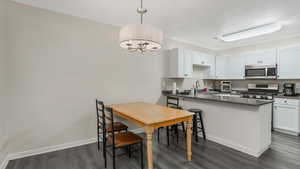 Kitchen with appliances with stainless steel finishes, dark wood-style floors, white cabinets, a peninsula, and a sink