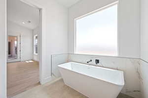 Bathroom featuring a soaking tub, tile walls, wood finished floors, and lofted ceiling