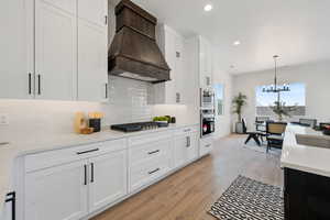 Kitchen featuring a chandelier, backsplash, light countertops, hanging light fixtures, and white cabinets