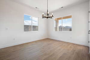 Spare room with a chandelier, wood finished floors, and baseboards
