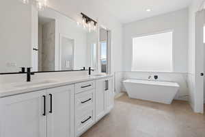 Full bathroom with a soaking tub, double vanity, tile walls, and a wainscoted wall