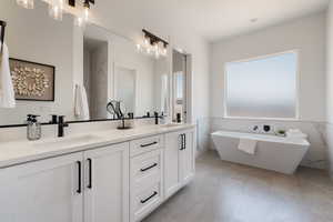 Full bath with double vanity, a freestanding bath, tile walls, and wainscoting