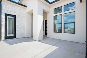 Doorway to property featuring stone siding, stucco siding, and a patio area