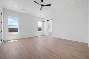 Unfurnished bedroom featuring a barn door, light wood-style floors, lofted ceiling, recessed lighting, and baseboards
