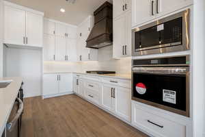 Kitchen with custom exhaust hood, appliances with stainless steel finishes, recessed lighting, light wood-type flooring, and white cabinetry
