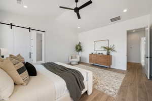 Bedroom featuring a barn door, wood finished floors, lofted ceiling, recessed lighting, and a ceiling fan