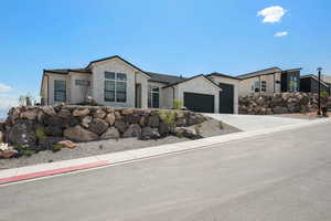 View of front of home with an attached garage, stone siding, concrete driveway, and stucco siding