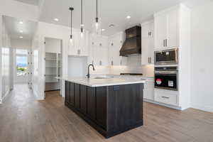 Kitchen featuring stainless steel appliances, a sink, custom range hood, baseboards, and light wood finished floors